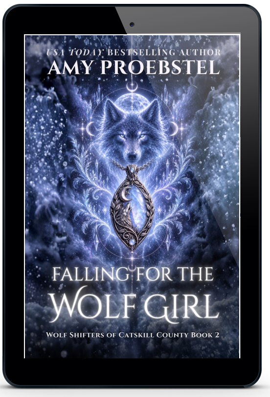 A black tablet device centered on a light gray background, displaying a book cover for 'Falling For the Wolf Girl' by Amy Proebstel. The cover art features a glowing blue wolf and a silver ring, with white title text.